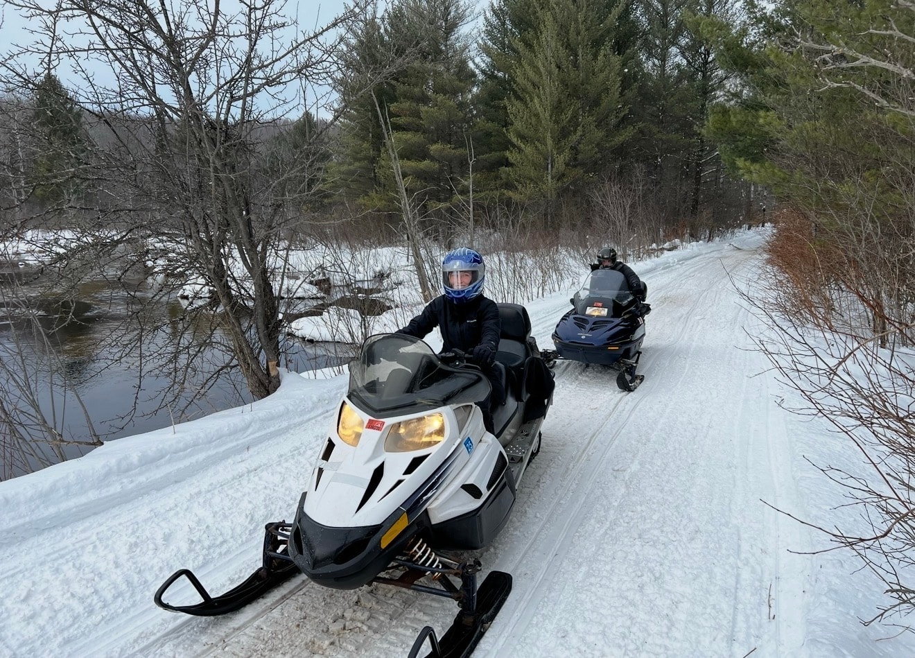 Two snowmobilers on a trail through the northern Michigan woods